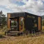 Modern tiny house on wheels in a natural rural landscape with wooden exterior and large windows